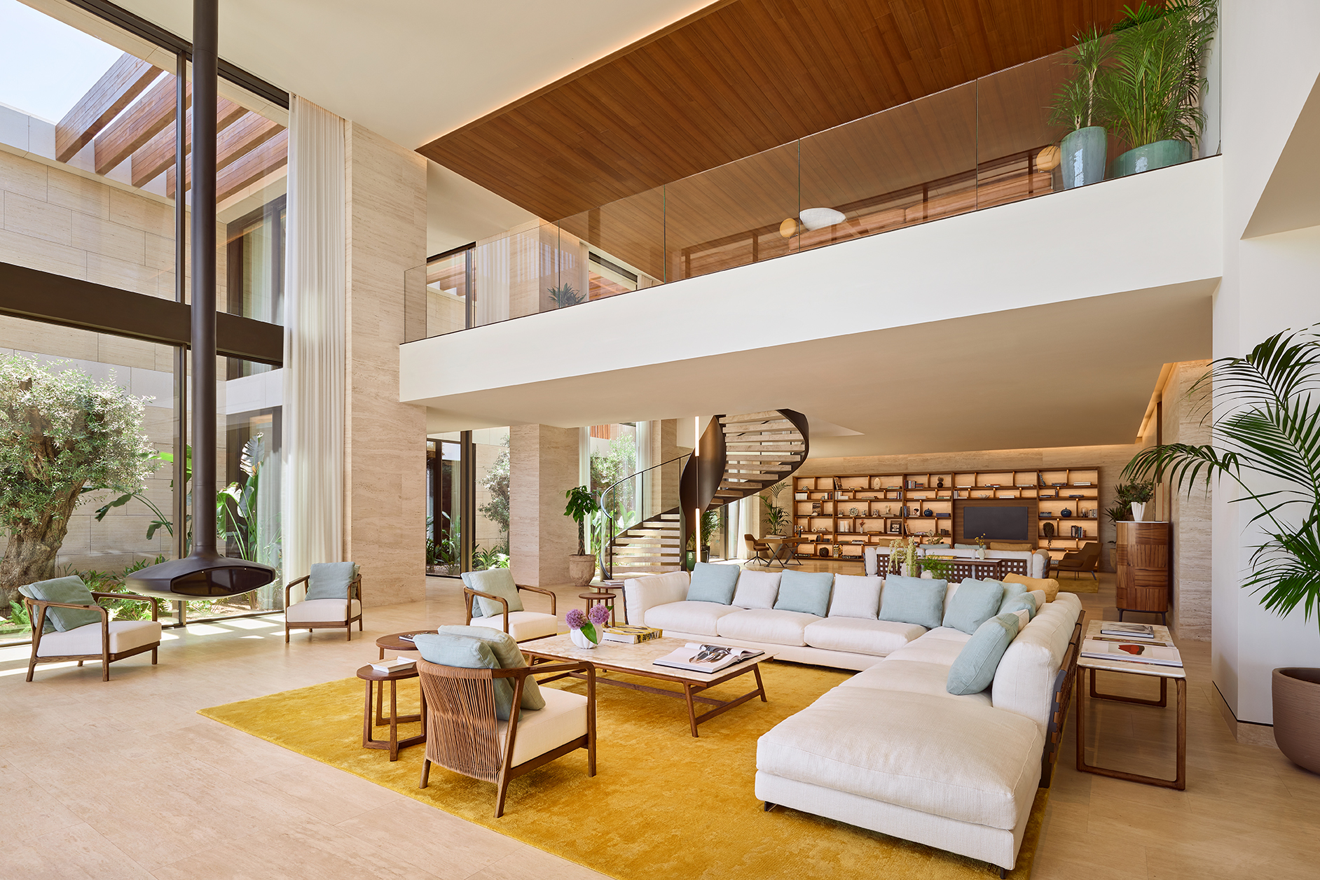 Interior shot of Bulgari Bodrum's Mansion Living Room with bright yellow carpet ,winding staircase to the upstairs, and suspended fireplace that creates an inviting atmosphere.